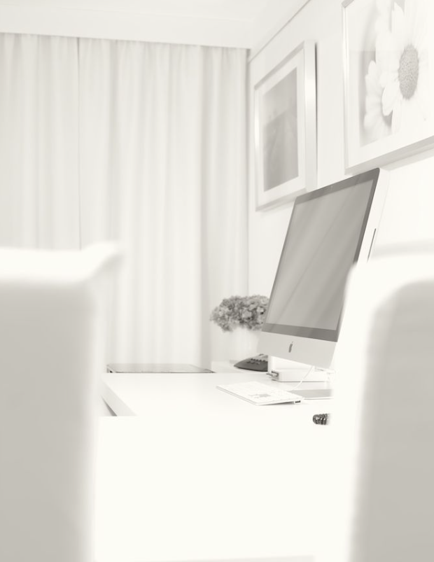 Raum für persönliche Beratung Heller Büroraum mit weißem Schreibtisch, Computer und Stühlen. Im Hintergrund hängen helle Vorhänge und gerahmte Blumenbilder.